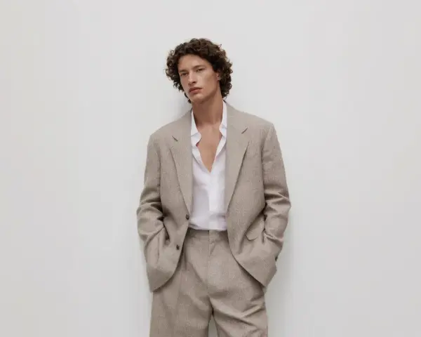 Uomo con capelli ricci indossa un completo beige, incarnando l'eleganza discreta dell'old money significato.
