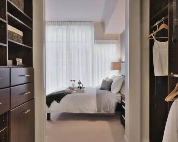 Dormitorio con vestidor integrado. Un espacio organizado con estanterías oscuras y cajones, que da paso a una cama acogedora y un armario con ropa colgada.