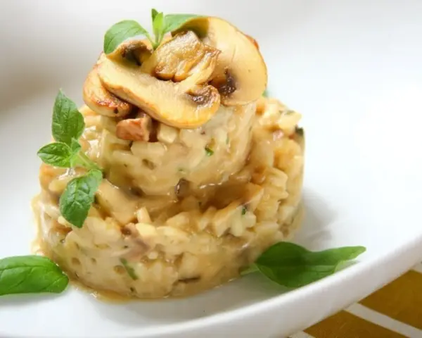 Kremowe risotto z grzybami, udekorowane listkami bazylii i oregano, prezentuje się apetycznie na białym talerzu.