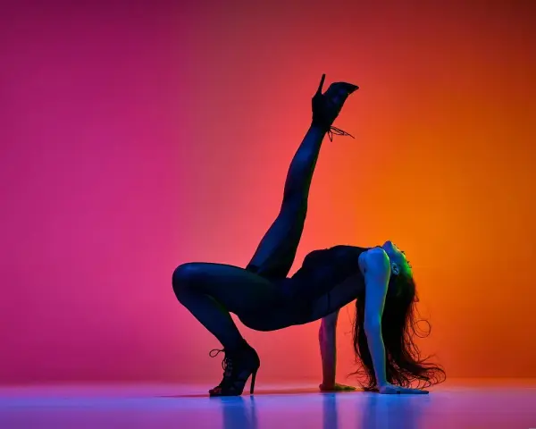 Tancerka w czarnym body i szpilkach wykonuje akrobatyczną figurę na tle gradientu różu i pomarańczy. High heels co to? To buty, które dodają pewności siebie.