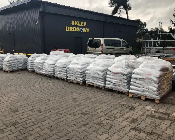 Palety z workami materiałów budowlanych przed sklepem drogowym.