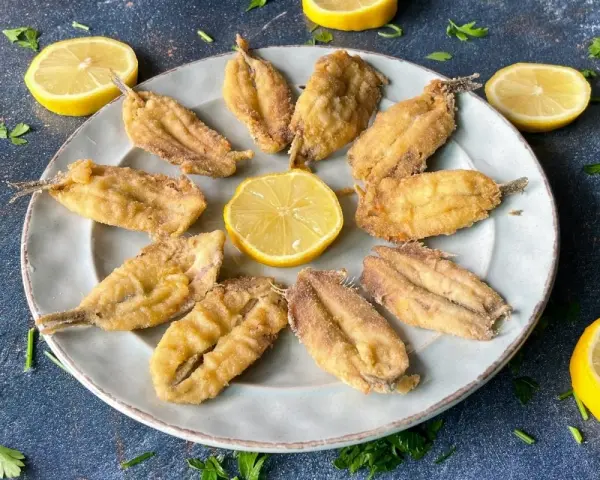 Deliciosos boquerones al limón, crujientes y dorados, servidos en un plato con rodajas de limón y perejil fresco.