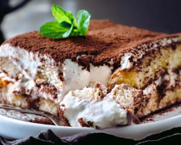 Tiramisú cremoso cubierto de cacao y decorado con menta.