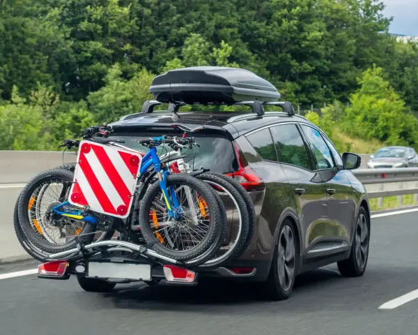 Auto in autostrada con due biciclette sul retro e box sul tetto. Il carico sporgente è ben visibile, pronto per un'avventura.