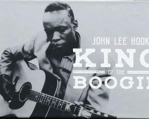 John Lee Hooker, King of the Boogie, spielt Gitarre. Sein Blick ist konzentriert, während seine Finger über die Saiten gleiten.