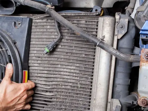 Mechanic inspects car's condenser, noting bent fins and corrosion, common symptoms of a bad condenser.