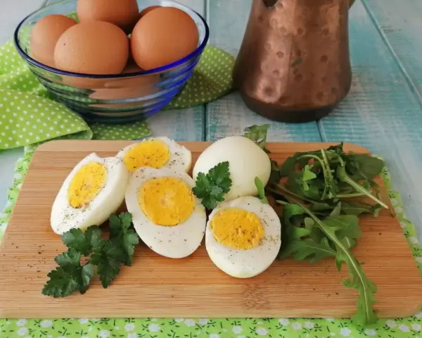 Uova sode in friggitrice ad aria, tagliate a metà, su tagliere con rucola e prezzemolo. Un modo sano e veloce per preparare le uova.