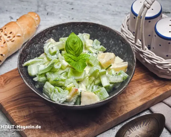 Ein cremiger sellerie salat mit frischem Basilikum, serviert in einer Schale neben einem Baguette und Salz- und Pfefferstreuern.