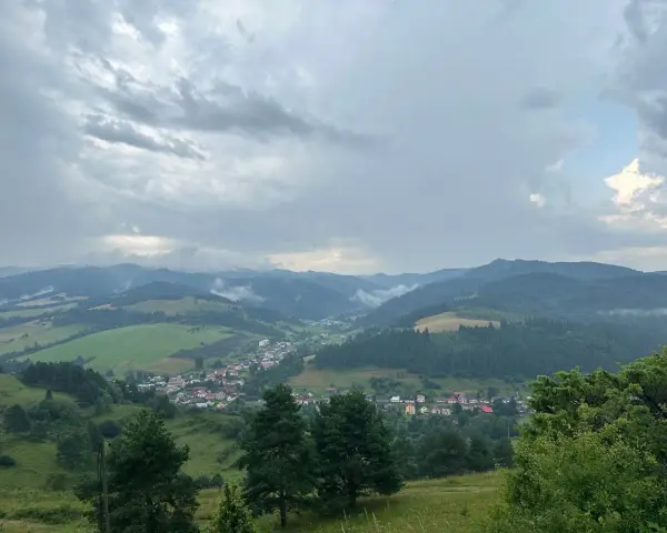 Malownicza panorama z widokiem na wieś w dolinie, otoczoną zielonymi wzgórzami i lasami. Nadciągają chmury, tworząc dramatyczne niebo nad lesnickie sedlo.