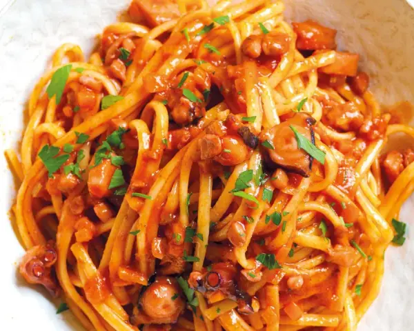Linguine al ragù di pesce, un piatto saporito con polpo e pomodoro, guarnito con prezzemolo fresco.