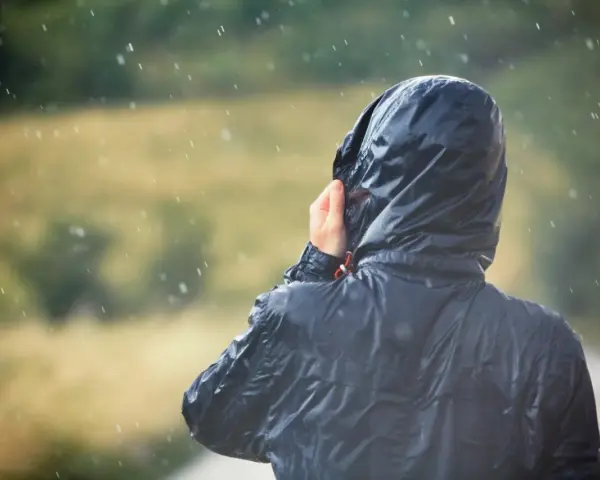 Person im Regen, die Kapuze einer Jacke mit PU-Beschichtung festhält.