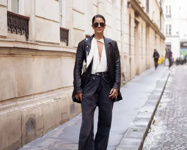 Mujer con gafas de sol y chaqueta de cuero, luciendo un elegante pantalón flare que es tendencia.