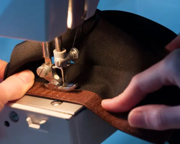 Mains habiles guidant un tissu noir sous une machine à coudre pour coudre du velcro marron.