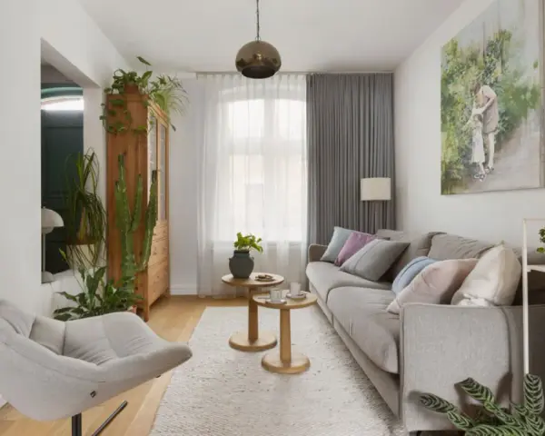 Przytulny salon w domu z szarą kanapą, wygodnym fotelem i mnóstwem zielonych roślin.