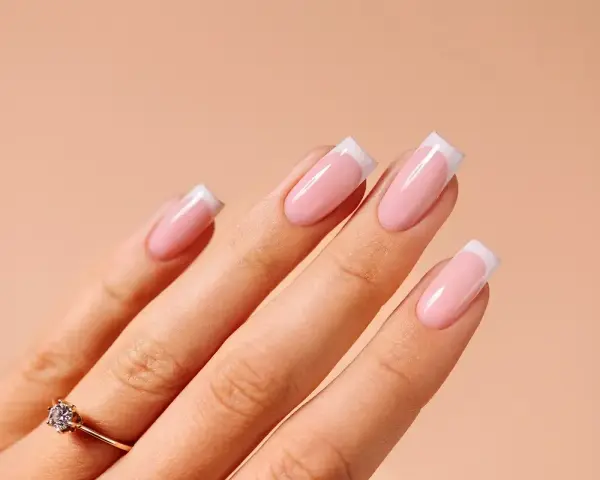 Dłonie z idealnym manicure french na paznokciach. Delikatny róż i biel tworzą klasyczny french na paznokciach, podkreślony subtelnym pierścionkiem.