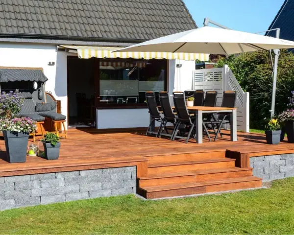 Eine 30 qm Terrasse gestalten: Holzdeck mit Sitzmöbeln, Esstisch, Sonnenschirm und Blumen. Perfekt für entspannte Stunden im Freien.