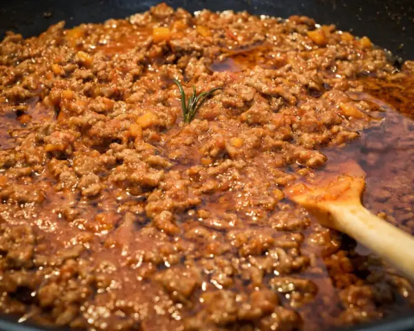 Un saporito ragù di lepre cuoce lentamente in padella, con un rametto di rosmarino che profuma l'aria.