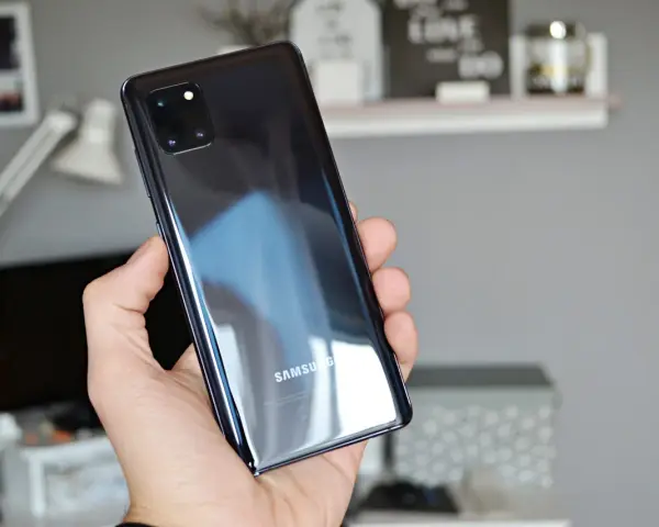 Dłoń trzyma błyszczący, czarny telefon Samsung A81 z modułem aparatów.