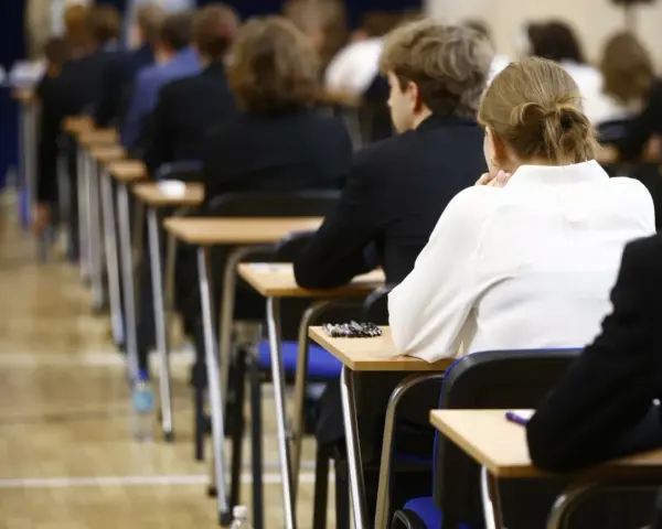 Uczniowie siedzą w rzędach przy ławkach, skupieni na rozwiązywaniu pytań maturalnych.