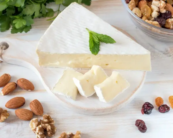 Queso brie en cuña y trozos, decorado con menta. Alrededor hay almendras, nueces y frutos secos. Ideal para quienes buscan información sobre queso brie calorias.
