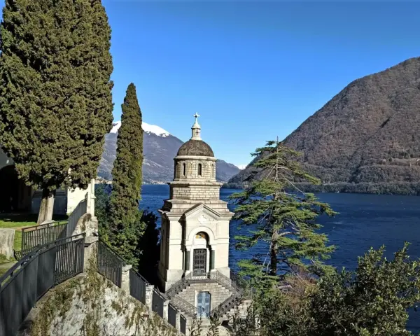 Un suggestivo lago con una piccola chiesa in mezzo, incorniciata da cipressi e montagne innevate.