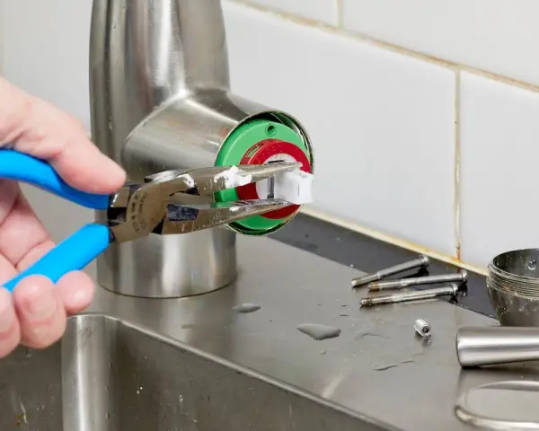 A hand uses pliers to remove a faucet cartridge, a key step in learning how to replace faucet cartridge.