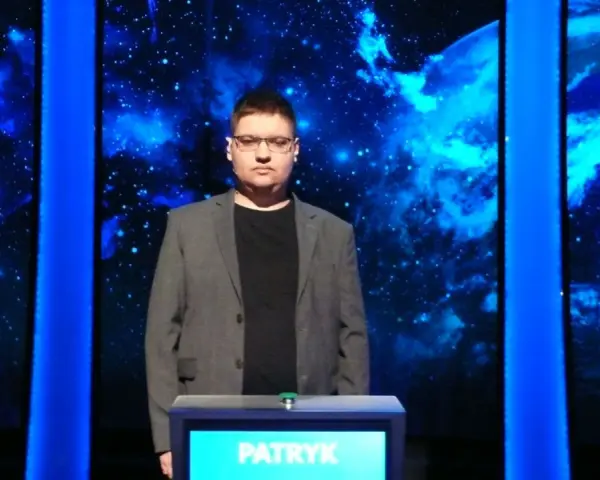 Patryk w szarym garniturze stoi przed niebieskim tłem z gwiazdami.