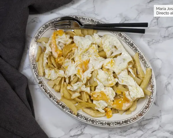 Plato de patatas fritas cubiertas con huevos rotos, con las yemas aún líquidas. Un clásico reconfortante.
