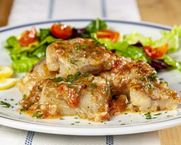 Deliziosa coda di rospo in umido con pomodoro e prezzemolo, servita con insalata fresca e spicchi di limone.