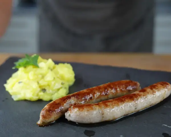 Zwei goldbraune Bratwürste mit Kartoffelsalat, perfekt für alle, die Bratwurst selber machen wollen.