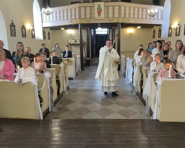 Uroczyste odnowienie przyrzeczeń chrzcielnych w kościele. Dzieci z zapalonymi świecami siedzą w ławkach, a ksiądz błogosławi zgromadzonych.