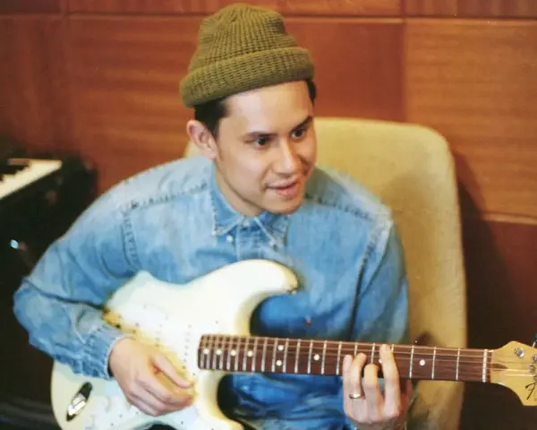 Frank Dukes w zielonej czapce i dżinsowej koszuli gra na gitarze Fender Stratocaster w studiu.