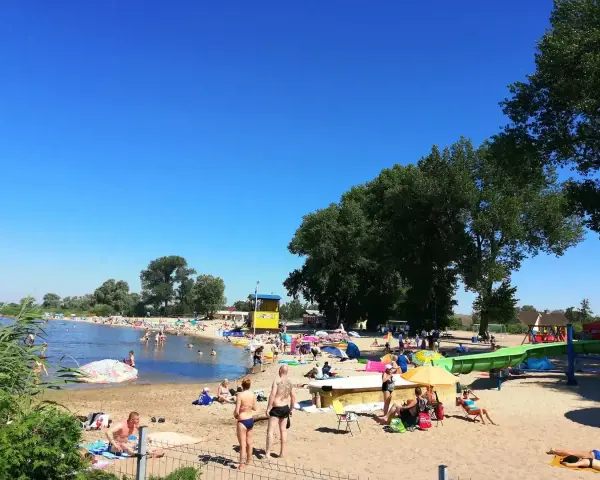 Słoneczny dzień na plaży, ludzie odpoczywają nad wodą. Zastanawiasz się, ile kilometrów jest ze Szczecina nad morze? To idealne miejsce na relaks przed podróżą.