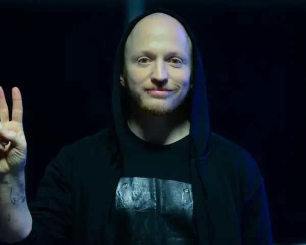 Wojtek Urbański w czarnej bluzie z kapturem pokazuje znak pokoju.