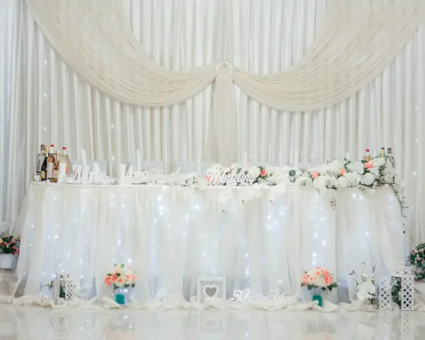 Elegancka ścianka za parą młodą inspiracje: białe zasłony, kwiaty, napisy "Wedding", "Love", "Mrs & Mr".