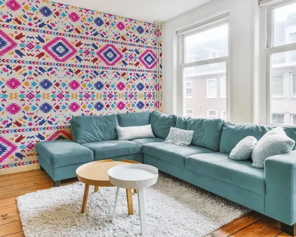 Un salon moderne avec un canapé bleu sarcelle et un papier peint intissé aux motifs ethniques colorés.