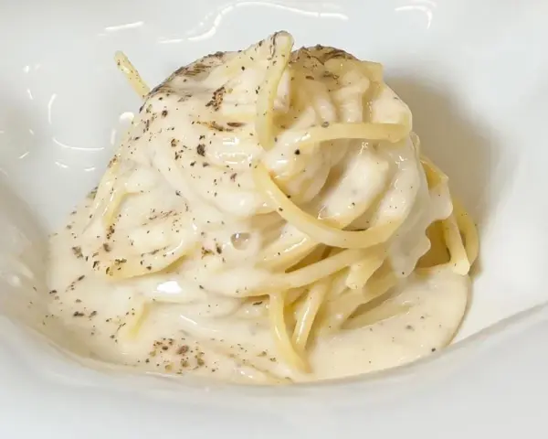 Un piatto di spaghetti cremosi, conditi con un'abbondante dose di cacio e pepe, cosparsi di pepe nero macinato.