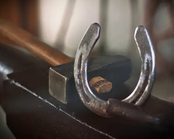 Un fer à cheval usé repose sur une enclume, à côté d'un marteau. L'artisanat du maréchal-ferrant est palpable.