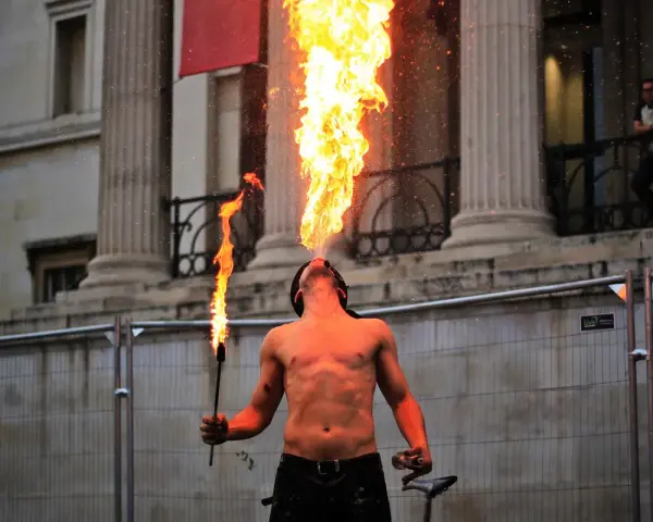 Feuerspucker bläst eine Flamme, während er eine Fackel hält. Der Mann brennt Vodka und zeigt seine Kunst vor einer beeindruckenden Säulenarchitektur.