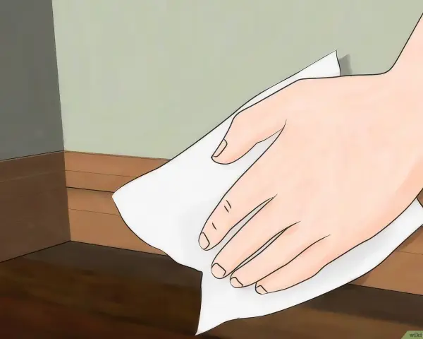Mano limpiando rodapiés de pintura con un paño blanco.