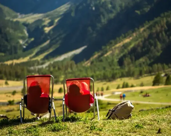 Dwie osoby w czerwonych leżakach podziwiają widok na Alpy w Austrii. Idealne miejsce na camping.