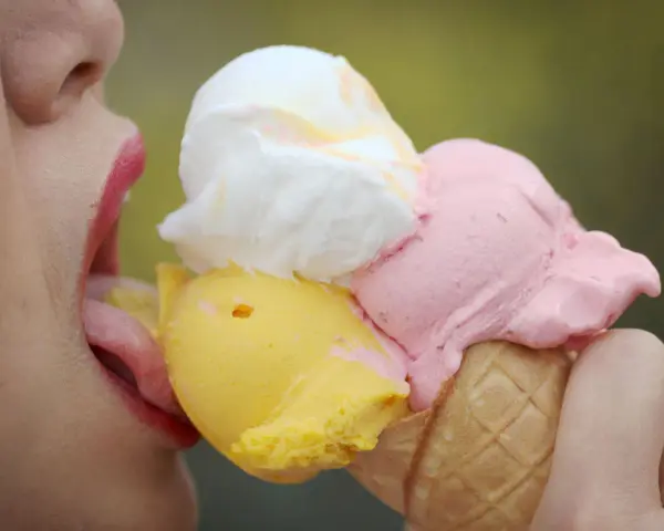 Eiscreme-Liebhaberin schleckt an einem Eis mit drei Kugeln. Die richtige guarkernmehl dosierung macht das Eis cremig.