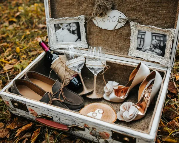 Elegancki prezent na ślub cywilny bez wesela: buty, wino, kieliszki, obrączki i zdjęcia pary w ozdobnej skrzyni.