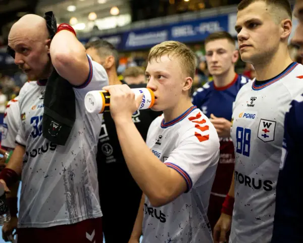 Szymon Adamczyk pije wodę z bidonu, otoczony kolegami z drużyny.