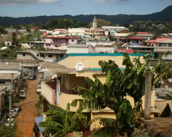 Vue d'une ville aux Comores, Mayotte, avec des maisons colorées, des bananiers et une montagne en arrière-plan.