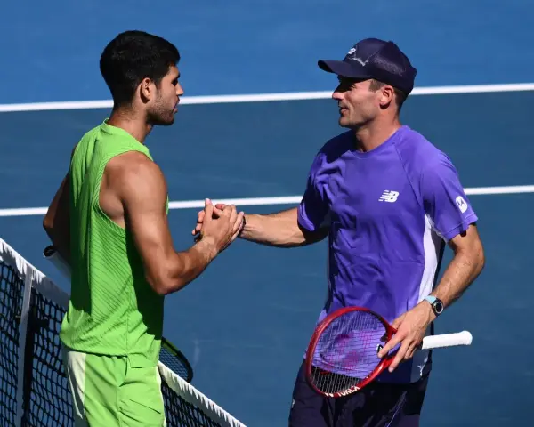 Dos tenistas, uno con camiseta verde y otro con morada, se dan la mano en la red. Tommy Paul, con gorra, sonríe tras el partido.