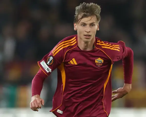 Piłkarz AS Roma w bordowej koszulce z żółtymi pasami, gotowy do gry przeciwko Genoa CFC.