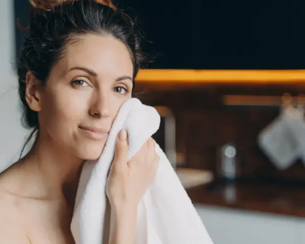 Une femme se sèche le visage avec une serviette. Elle a une peau radieuse, peut-être grâce aux 10 aliments bon pour la peau.