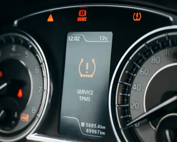 Na desce rozdzielczej świeci się kontrolka niskiego ciśnienia w oponach (TPMS). Obok widać wskaźnik hamulca i ostrzeżenie o temperaturze.