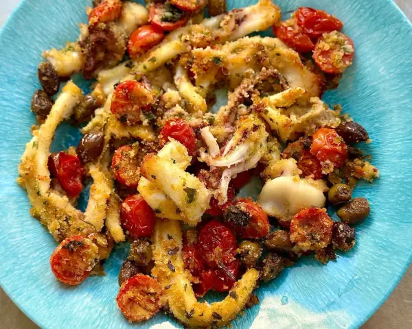 Calamari gratinati al forno su piatto blu, con pomodorini e olive.